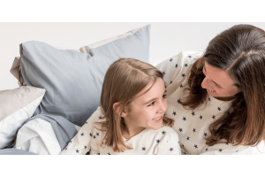 a woman and her daughter sitting on a bed in Zizzz pajamas