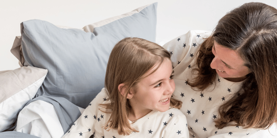 a woman and her daughter sitting on a bed in Zizzz pajamas