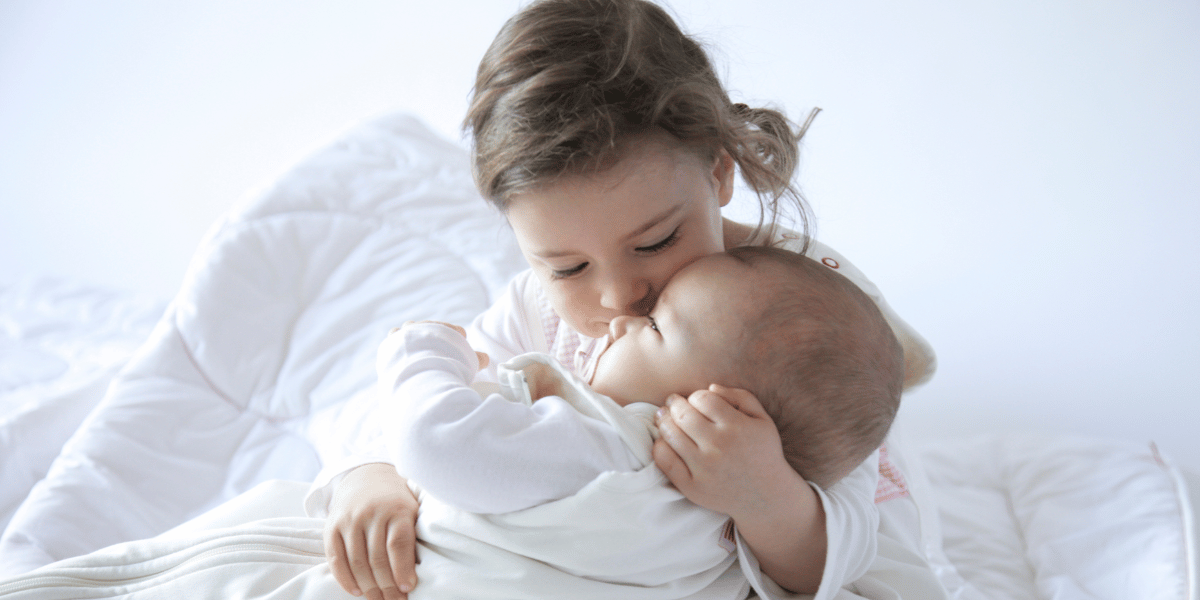 Petite fille qui tient un bébé en gigoteuse dans ses bras